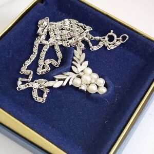 May include: A silver necklace with a grape cluster pendant featuring faux pearls and rhinestones. The necklace is in a blue velvet box with a gold trim.