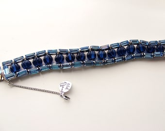 Può includere: Un braccialetto vintage con file alternate di perline blu e azzurre rettangolari e sferiche. Il braccialetto ha una chiusura color argento e una catena di sicurezza con una piccola etichetta attaccata.