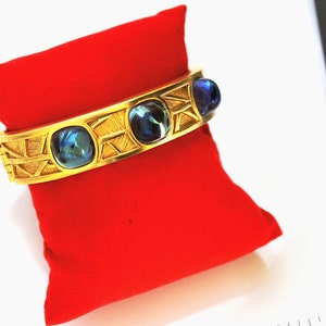 Puede incluir: Un brazalete de oro con tres cabujones de concha de abulón azul engastados en un diseño geométrico.