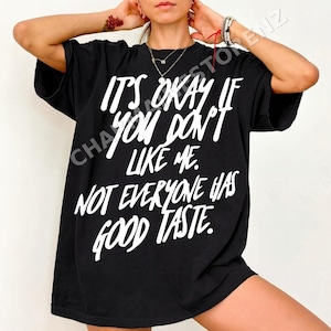 May include: Black oversized t-shirt with white text: "IT'S OKAY IF YOU DON'T LIKE ME. NOT EVERYONE HAS GOOD TASTE." The tee has short sleeves and a loose fit. A casual, statement piece.