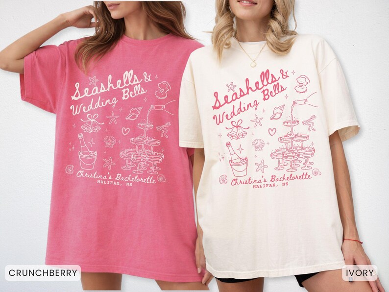 K&ouml;nnte beinhalten: Zwei &uuml;bergro&szlig;e T-Shirts, eines in Crunchberry und das andere in Elfenbein, zeigen ein wei&szlig;es Grafikdesign. Das Design enth&auml;lt den Text "Seashells & Wedding Bells" und Illustrationen von Champagner, Muscheln und einem Champagnerturm. Der Text "Christina's Bachelorette, Halifax, NS" ist ebenfalls enthalten.