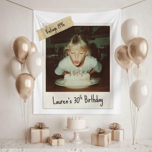 Puede incluir: Una pancarta de cumpleaños con una foto vintage de una persona soplando las velas de un pastel. La pancarta dice "Lauren's 30th Birthday" y "Vintage 1996". Globos y regalos envueltos decoran la escena.