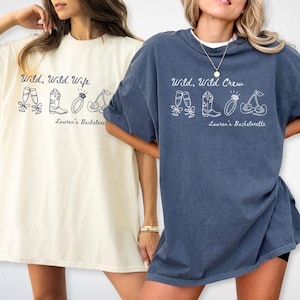 Puede incluir: Dos camisetas de gran tama&ntilde;o, una marfil y otra azul vaquero, con los textos "Wild, Wild Wife" y "Wild, Wild Crew" y gr&aacute;ficos relacionados. Las camisetas forman parte de una colecci&oacute;n de despedida de soltera.