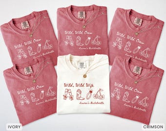 Puede incluir: Una colección de camisetas carmesí y marfil con las frases "Wild, Wild Crew" y "Wild, Wild Wife". Cada camiseta presenta un collar y un gráfico de copas de champán, botas, un anillo y cerezas. Son camisetas para una despedida de soltera.