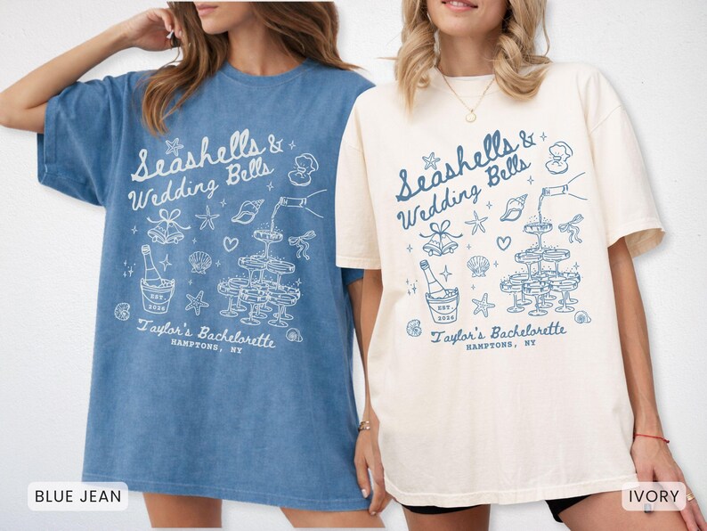 K&ouml;nnte beinhalten: Zwei T-Shirts, eines in Jeansblau und eines in Elfenbein, mit einem grafischen Design. Das Design enth&auml;lt den Text "Seashells & Wedding Bells" und "Taylor's Bachelorette, Hamptons, NY" sowie Muscheln, Sektgl&auml;ser und eine Flasche.