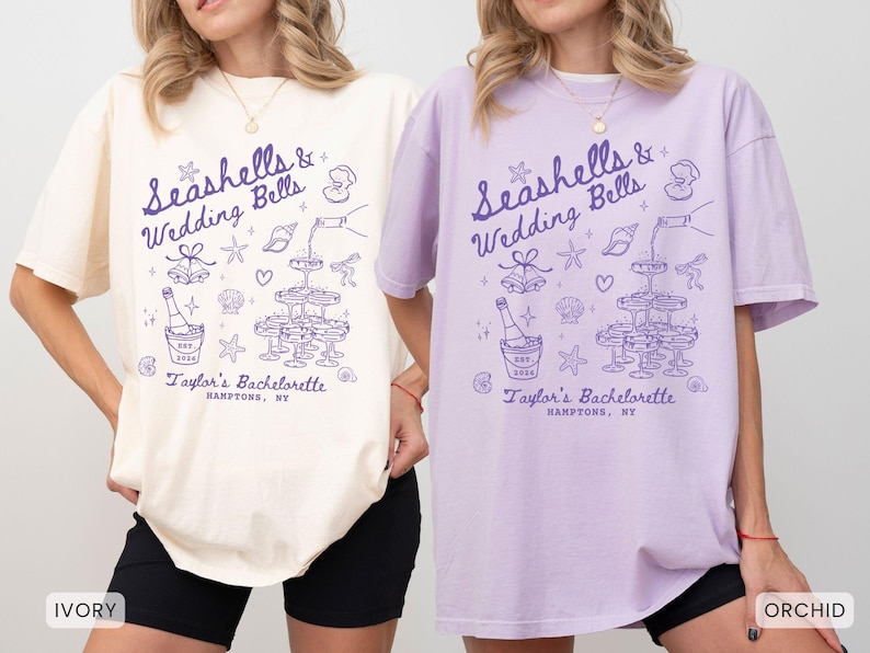 K&ouml;nnte beinhalten: Elfenbein- und orchideenfarbene T-Shirts mit einem lila Grafikdesign. Das Design enth&auml;lt den Text "Seashells & Wedding Bells" und "Taylor's Bachelorette, Hamptons, NY" sowie Illustrationen von Sektgl&auml;sern, Muscheln und einer Sektflasche.