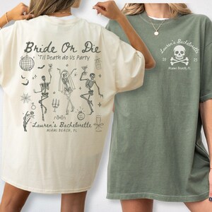 May include: Two t-shirts, one ivory, one moss green. The ivory shirt has a skeleton design with the text "Bride Or Die" and "Lauren's Bachelorette, Miami Beach, FL." The moss shirt features a skull and crossbones design with the text "Lauren's Bachelorette, Miami Beach, FL."