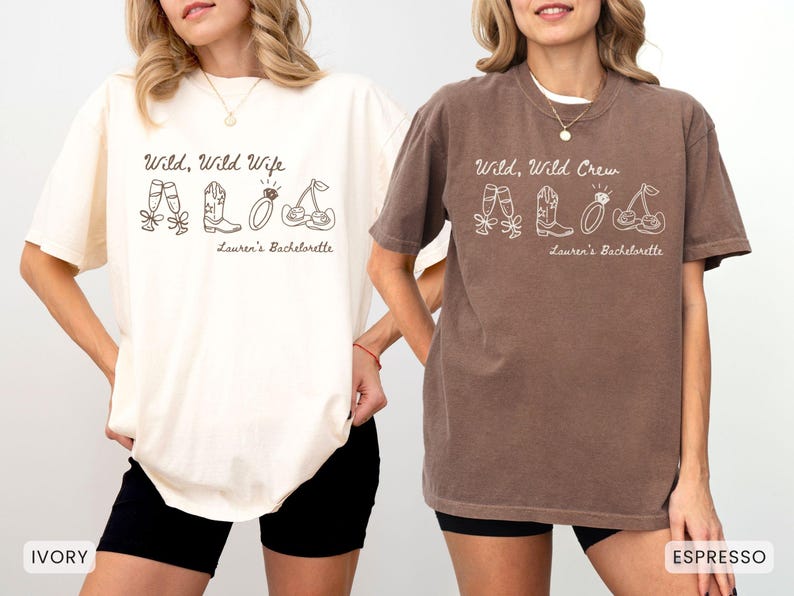 Puede incluir: Dos camisetas, una marfil y otra espresso, con el texto "Wild, Wild Wife" y "Wild, Wild Crew" en letra cursiva. Cada camiseta tiene un dibujo lineal de zapatillas de ballet, botas de vaquero, un anillo y cerezas. "Lauren's Bachelorette" est&aacute; debajo.