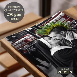 May include: A black and white photographic print on 250 gsm (110 lb) premium quality paper. The image depicts a person with a green and yellow mohawk hairstyle kissing a person wearing a black and white habit. A red bus is visible in the background.
