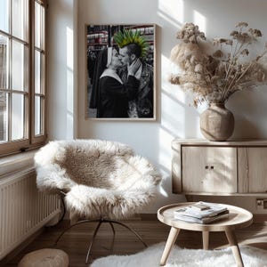 May include: A framed black and white photograph hanging on a wall, depicting a nun kissing a person with a bright green mohawk hairstyle. The person with the mohawk wears a black leather jacket with metal studs, while the nun wears a traditional habit.