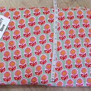 May include: A folded fabric with a repeating floral pattern in red, orange, and white on a light green background. A measuring tape is laid across the fabric. The tag says TEXTILECITY Store.