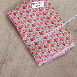 May include: A folded fabric with a repeating floral pattern in red and orange on a light green background. A measuring tape is laid across the fabric. The label "TEXTILECITY Store" is visible.