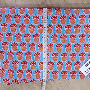 May include: Folded fabric with a repeating pattern of orange and red floral designs on a light blue background. A measuring tape is placed on top of the fabric. The tag says TEXTILECITY Store.