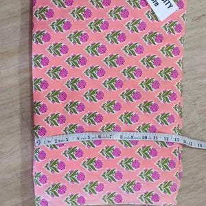 May include: Pink fabric with a repeating floral pattern in pink and green. A measuring tape is laid across the fabric. The tag reads TEXTILECITY Store.