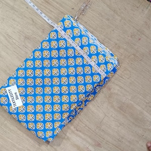 May include: A folded blue fabric with a repeating yellow floral pattern, measured with a white measuring tape. The fabric has a tag that reads "TEXTILECITY STORE". The fabric is on a light brown wooden surface.