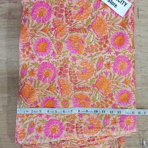 May include: A folded fabric with a floral pattern in shades of pink, orange, and green. The fabric is measured with a tape measure. The tag says TEXTILECITY Store.