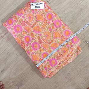May include: A folded fabric with a floral pattern in shades of pink and orange. The fabric is being measured with a ruler. The text "TEXTILECITY Store" is visible on a white label.