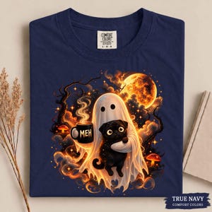 May include: A navy blue t-shirt featuring a graphic of a white ghost holding a black mug with the text MEH and hugging a black pug. The scene includes a large orange moon, dark tree branches, glowing stars, and small orange mushrooms.