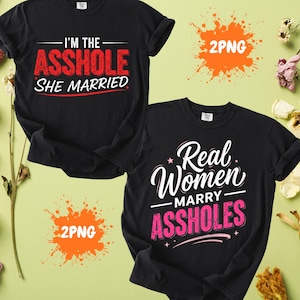 May include: Two black t-shirts with humorous text. One reads "I'M THE ASSHOLE SHE MARRIED" in red and white. The other says "Real Women MARRY ASSHOLES" in white and pink. Both shirts have rolled sleeves.
