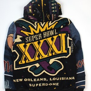 Op de afbeelding: Een zwarte hoodie met een geweven afbeelding voor Super Bowl XXXI in New Orleans, Louisiana. Het ontwerp bevat een grote gele kroon, de tekst 'SUPER BOWL XXXI', 'NEW ORLEANS, LOUISIANA' en 'SUPERDOME' met kleurrijke confetti-accenten.