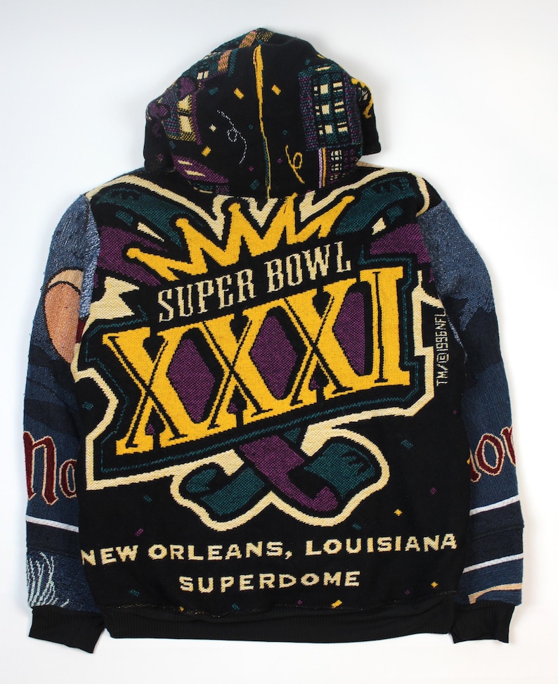Op de afbeelding: Een zwarte hoodie met een geweven afbeelding voor Super Bowl XXXI in New Orleans, Louisiana. Het ontwerp bevat een grote gele kroon, de tekst 'SUPER BOWL XXXI', 'NEW ORLEANS, LOUISIANA' en 'SUPERDOME' met kleurrijke confetti-accenten.