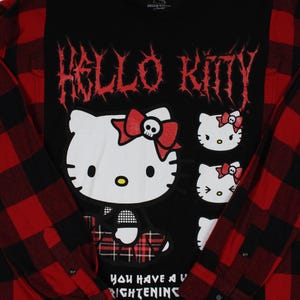 May include: Black long-sleeved shirt with a red and black plaid pattern on the sleeves. The shirt features a graphic of Hello Kitty with a skull bow and the text "Hello Kitty" in red. The shirt also has the text "You have a frightening" on the bottom.