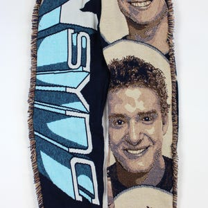 May include: Woven navy blue sweatpants with a light blue and white graphic design on one leg and a portrait on the other. The sweatpants have a drawstring waist and fringed edges.