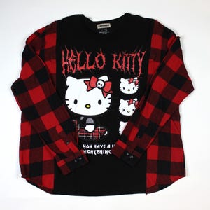May include: Black long-sleeved shirt with a red and black plaid pattern on the sleeves. The front features a Hello Kitty graphic with the text "HELLO KITTY" in a gothic font. The shirt also has the text "YOU HAVE A LIGHTENING".