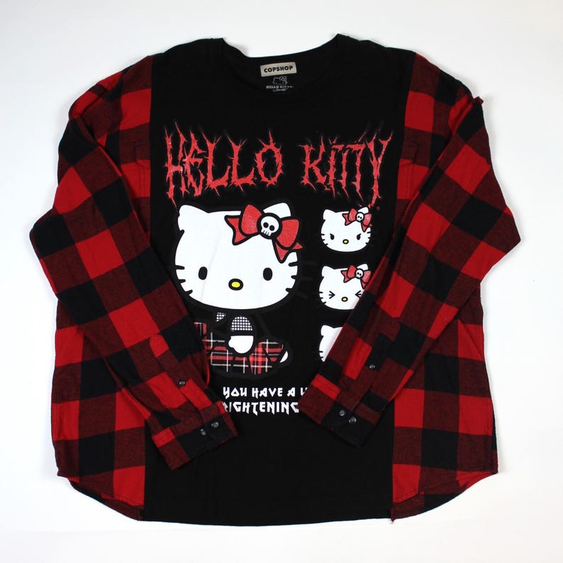 May include: Black long-sleeved shirt with a red and black plaid pattern on the sleeves. The front features a Hello Kitty graphic with the text "HELLO KITTY" in a gothic font. The shirt also has the text "YOU HAVE A LIGHTENING".