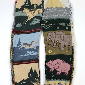 May include: Tapestry trousers with a drawstring waist and fringed edges. The design features scenes of a horse and rider, a running dog, elephants, pigs, and a sunrise. The colour palette includes beige, green, blue, and red.