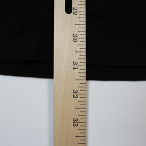 May include: Close-up of a black fabric with a wooden ruler. The ruler is marked with inch measurements from 29 to 33. The fabric is smooth and appears to be a solid color. The background is white.