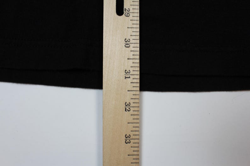 May include: Close-up of a black fabric with a wooden ruler. The ruler is marked with inch measurements from 29 to 33. The fabric is smooth and appears to be a solid color. The background is white.