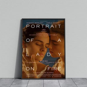 May include: A framed movie poster for "Portrait of a Lady on Fire." The poster features two women with their faces close together. The title is at the top, with the film's name and director's name at the bottom. The poster has a dark frame.