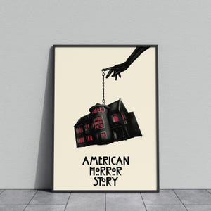 Może przedstawiać: Oprawiony plakat z mroczną ilustracją domu zawieszonego na łańcuchu trzymanym przez czarną rękę. Dom ma czerwone podświetlane okna. Słowa "AMERICAN HORROR STORY" są wydrukowane na czarno poniżej.