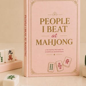 Puede incluir: Un libro de tapa dura rosa titulado People I Beat at Mahjong con letras doradas, acompañado de fichas de mahjong blancas con símbolos rojos y verdes, y dos libros adicionales en verde y crema con las palabras Ambitious y Collective.