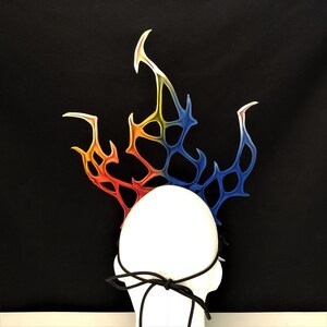 May include: A white headband with a colorful, flame-shaped design. The headband is made of a flexible material and has a black elastic band.