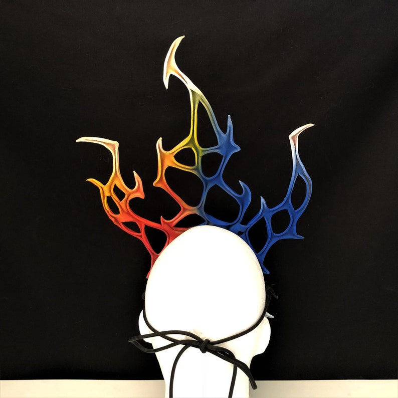 May include: A white headband with a colorful, flame-shaped design. The headband is made of a flexible material and has a black elastic band.