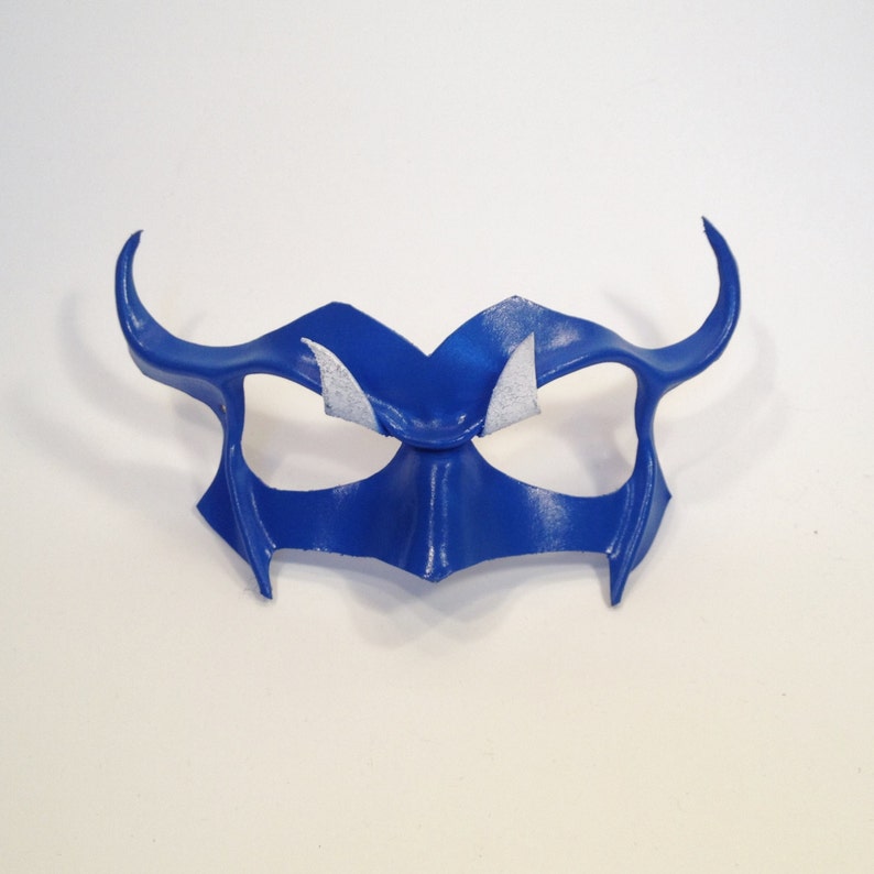 May include: A blue leather masquerade mask with white accents. The mask has a pointed, angular design and eye holes.