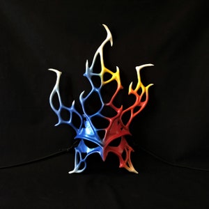 May include: A blue, red, and yellow masquerade mask with a flame-like design. The mask is made of a lightweight material and has a delicate, intricate design.