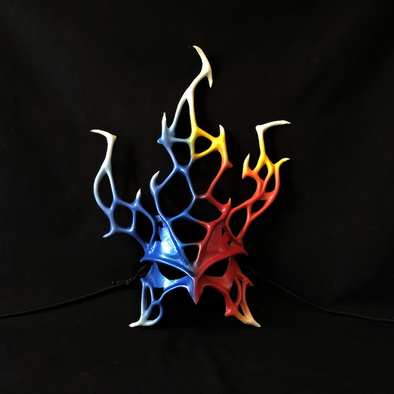 May include: A blue, red, and yellow masquerade mask with a flame-like design. The mask is made of a lightweight material and has a delicate, intricate design.