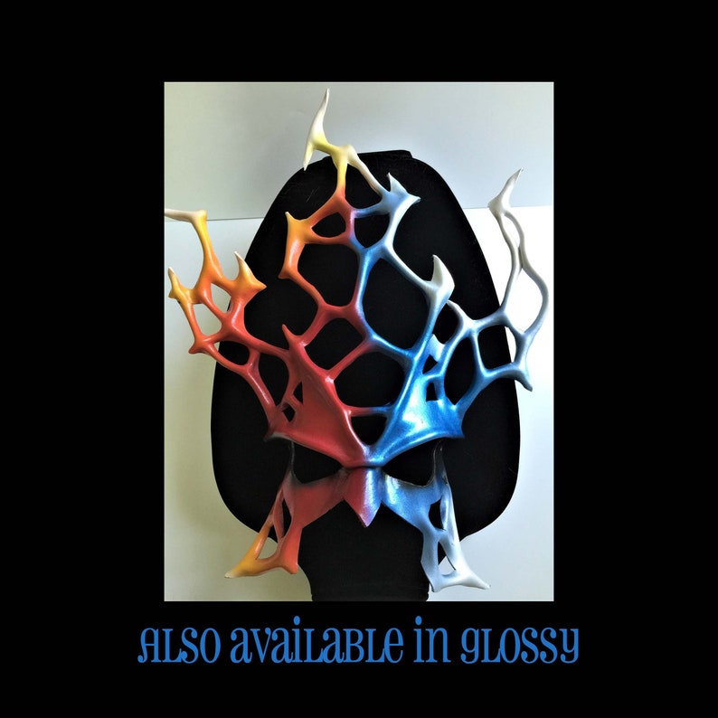May include: A colorful, abstract mask with a web-like design. The mask is made of a hard material and is painted in shades of red, orange, yellow, blue, and white.