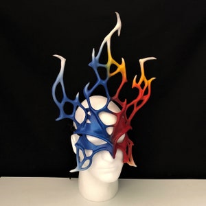 May include: A blue and red masquerade mask with a white, yellow, and orange flame design. The mask is made of a lightweight material and has a delicate, intricate design.