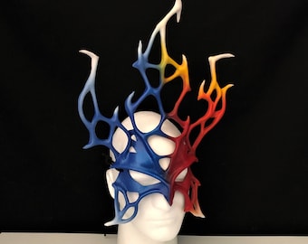 May include: A blue and red masquerade mask with a white, yellow, and orange flame design. The mask is made of a lightweight material and has a delicate, intricate design.