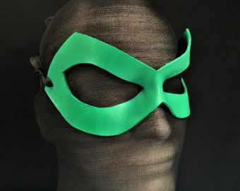 Può includere: Una maschera per gli occhi verde con un tessuto nero che copre la testa. La maschera ha una forma semplice e arrotondata con un solo foro per l'occhio.