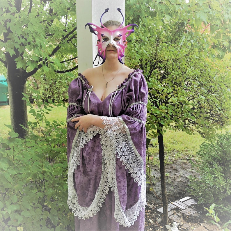 May include: A woman wearing a purple dress with lace trim and a pink butterfly mask. The dress has a low neckline and the mask has intricate details.