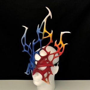 May include: A red, blue, and yellow leather mask with a flame-like design. The mask is on a white mannequin head.