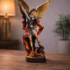 Pode incluir: Uma estatueta detalhada de São Miguel Arcanjo, retratado com asas douradas e uma espada de prata, em pé sobre uma figura derrotada. A estátua apresenta uma mistura de cores, incluindo ouro, prata, vermelho e branco, e está sobre uma base preta.