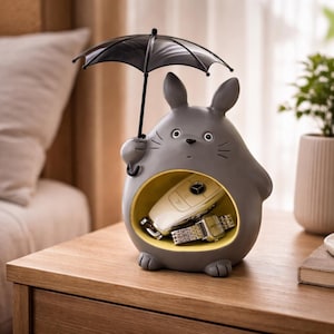 Puede incluir: Figura gris con forma de conejo de dibujos animados sosteniendo un paraguas negro. El conejo tiene un compartimento interior amarillo que contiene una llave de coche y un reloj. La figura está sobre una superficie de madera.