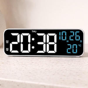 Könnte beinhalten: Ein rechteckiger digitaler Wecker mit schwarzem Display und weißen und blauen Ziffern. Die Uhrzeit zeigt 20:38 an, mit Datum und Temperatur. Die Uhr hat einen silbernen Rahmen und zwei Wecker-Symbole.