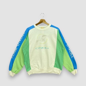 Puede incluir: Sudadera O'Neill color crema con detalles en azul y verde. Las mangas son azules y verdes, con el texto "TEAM O'NEILL" impreso verticalmente. La parte delantera presenta el logotipo de O'Neill y un gr&aacute;fico de p&aacute;jaro.